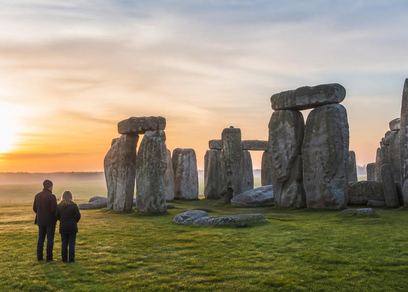 Two visitors standing quietly at Stonehenge in the early morning light